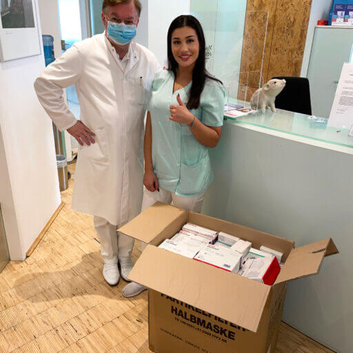 Dr. Dr. Bieniek und seine Mitarbeiterin mit einem Hilfspaket für die Ukraine im Flur der Zahnarztpraxis